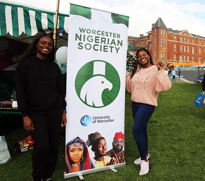 a photo of two smiling students in front of the Nigerian Society banner