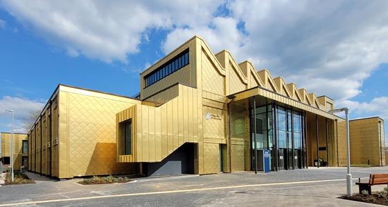 Exterior view of the Elizabeth Garrett Anderson building. It is a gold-clad building. The sky is blue with a few clouds.
