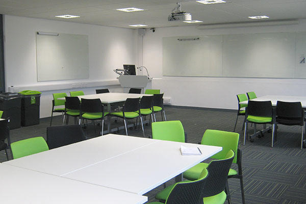 A lecture room with green chairs and white tables