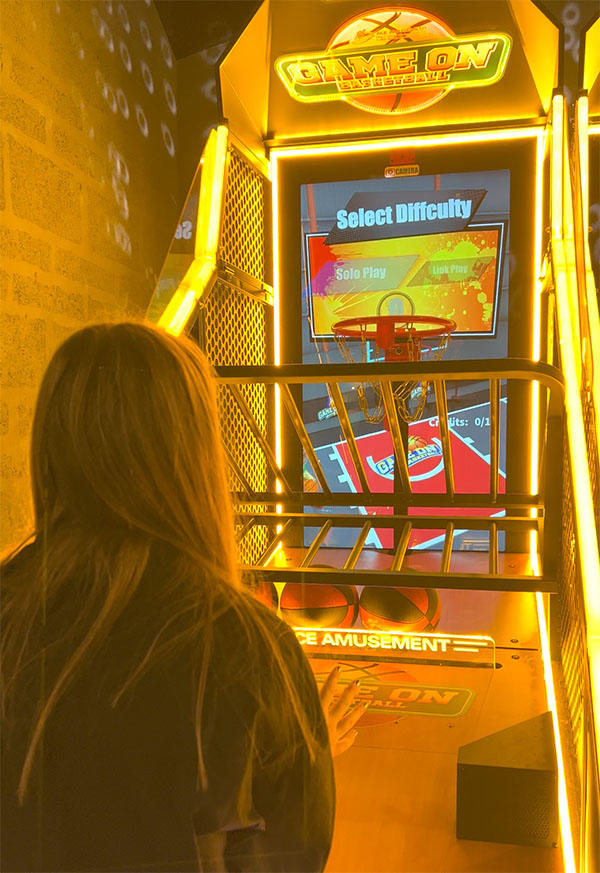 Back of woman's upper body playing arcade basketball with neon yellow light